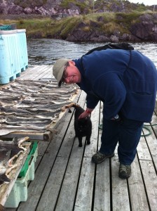 Sara Stratton petting a black cat at a fish flake in Southport, Trinity Bay, Newfoundland.