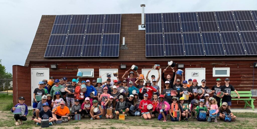 Group of happy children and leaders in front of a roof with solar panels