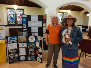 Two women standing in front of a display, one in an orange shirt, the other in a ribbon skirt.