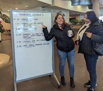 Two women standing next to a white board

Description automatically generated